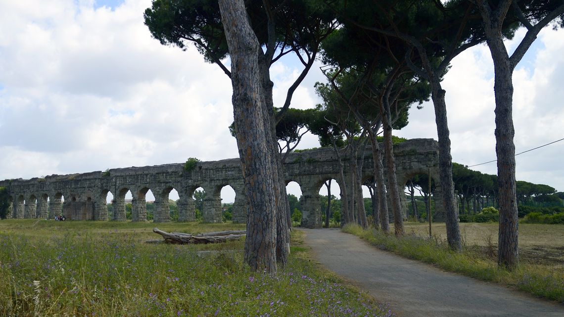 Le arcate dell'acquedotto Claudio nel Parco degli Acquedotti, con i pini a ombrello in primo piano e un sentiero sterrato che corre lungo il prato