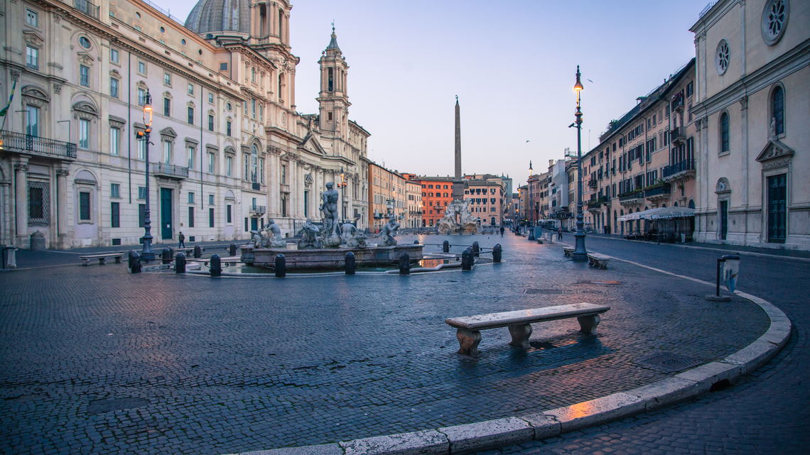 Piazza Navona all'alba, vuota: la fontana del Moro, l'obelisco e Sant'Agnese in Agone, i lampioni ancora accesi