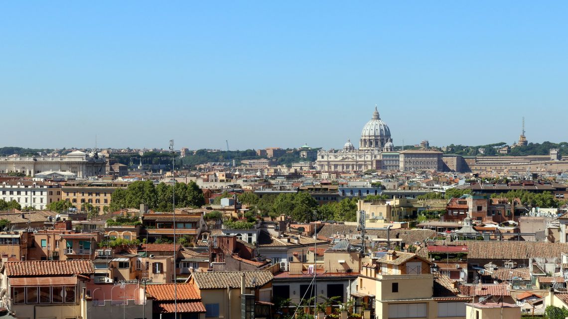 I tetti di Roma visti dall'alto: coppi di terracotta, terrazze con le piante e antenne, e in fondo la cupola di San Pietro sopra la città