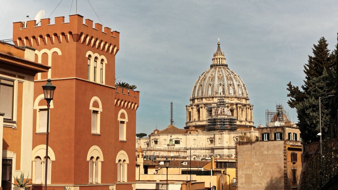 La cupola di San Pietro sopra i tetti, con una torretta di intonaco arancio in primo piano
